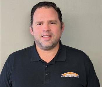 Male Employee with black polo standing in front of tan background